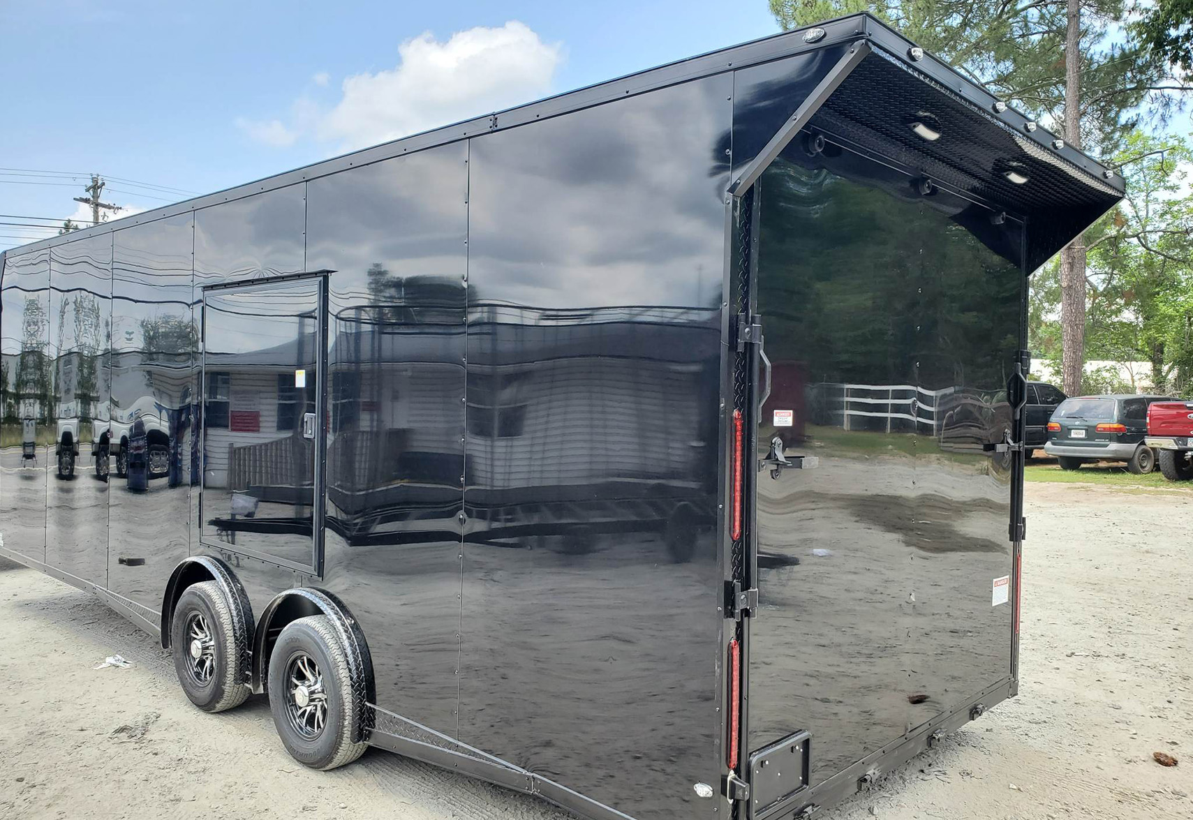 The image depicts a large black trailer with a closed door, parked on what appears to be an asphalt surface.