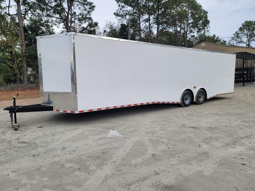 The image features a large white box trailer parked on a gravel surface.