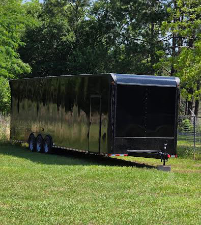 The image shows a large black enclosed trailer parked on grass.