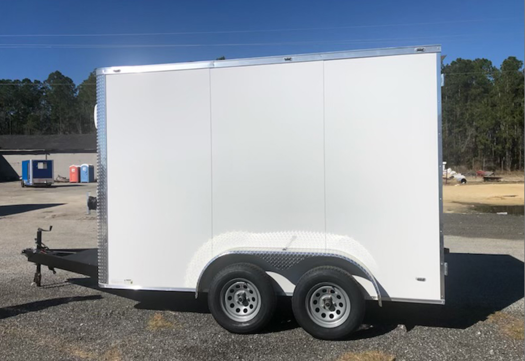 A white enclosed trailer is parked on a gravel surface.