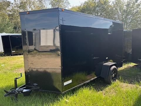 The image shows a large, black enclosed trailer parked on grass.