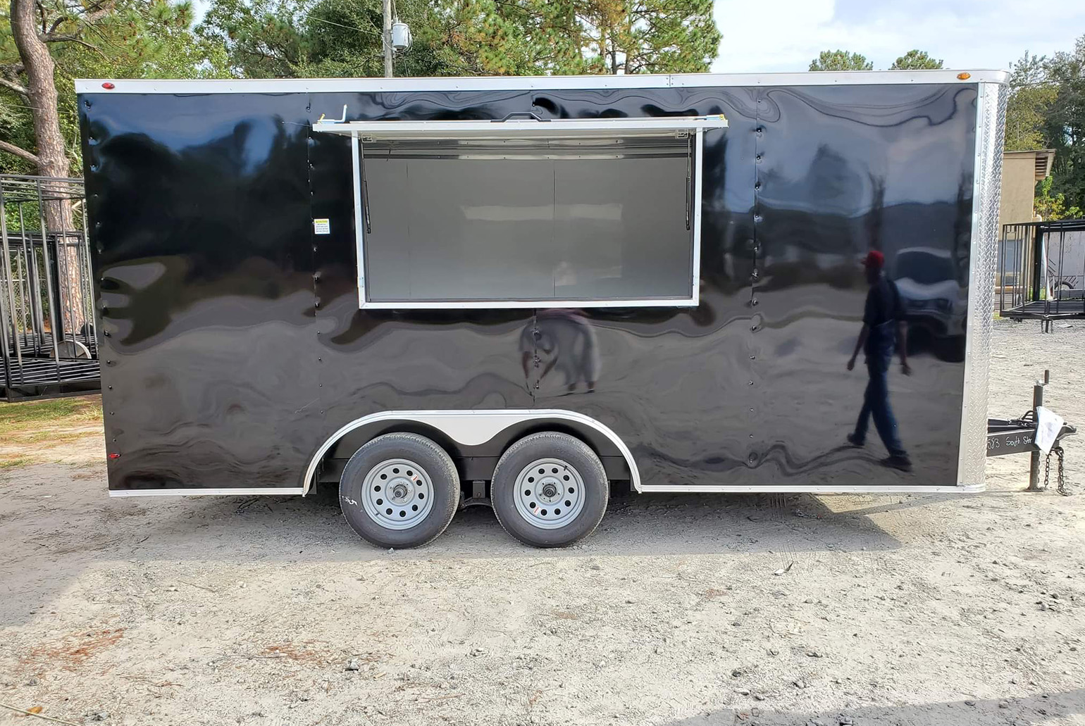 The image shows a black food truck parked on a paved surface, with a person visible in the background.