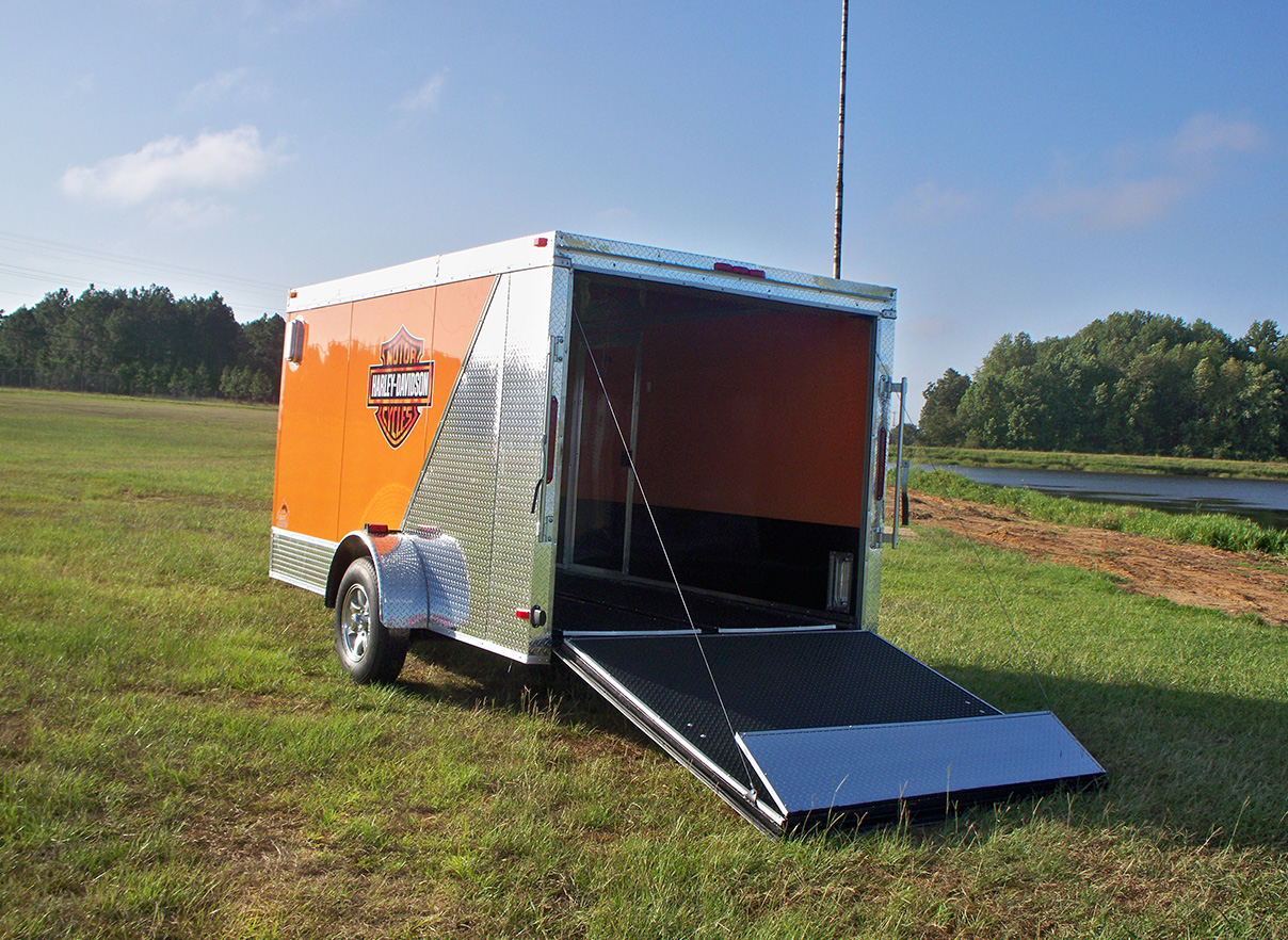 An orange and white trailer with a lift-up door, parked on grass in an open field.